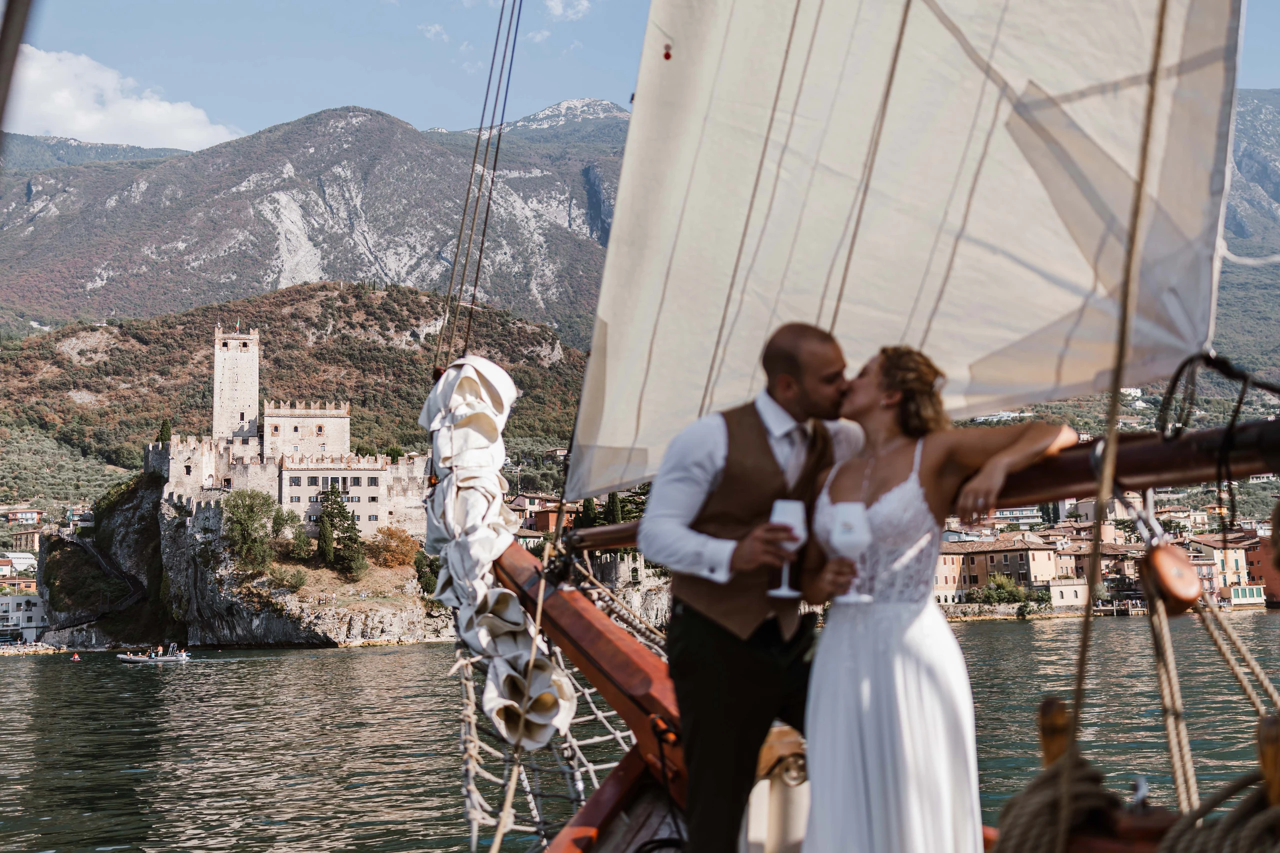 Brautpaar auf einem Segelboot mit historischer Burg und Bergen am Gardasee