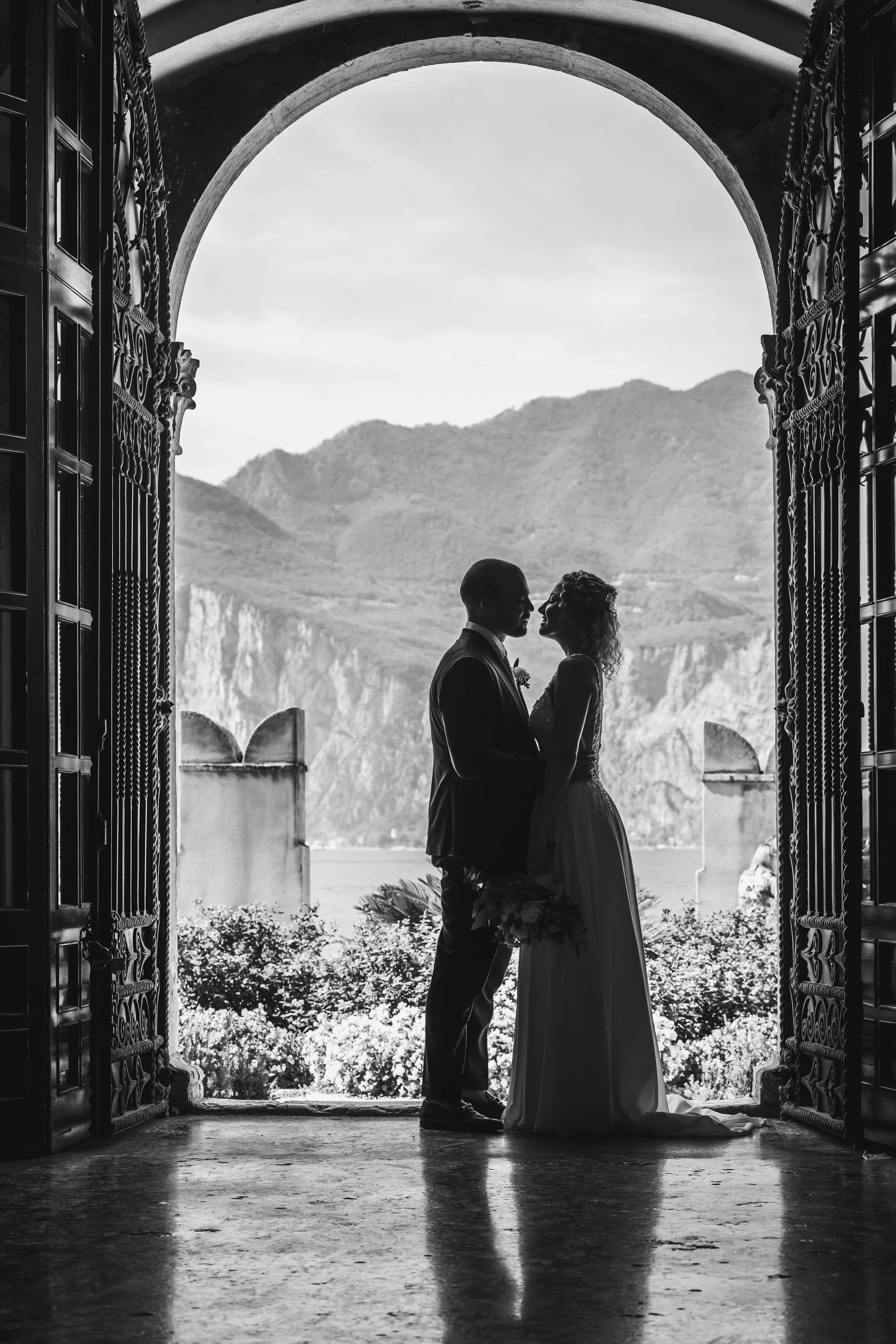 Silhouette eines Brautpaars in einem historischen Torbogen mit Bergblick am Gardasee
